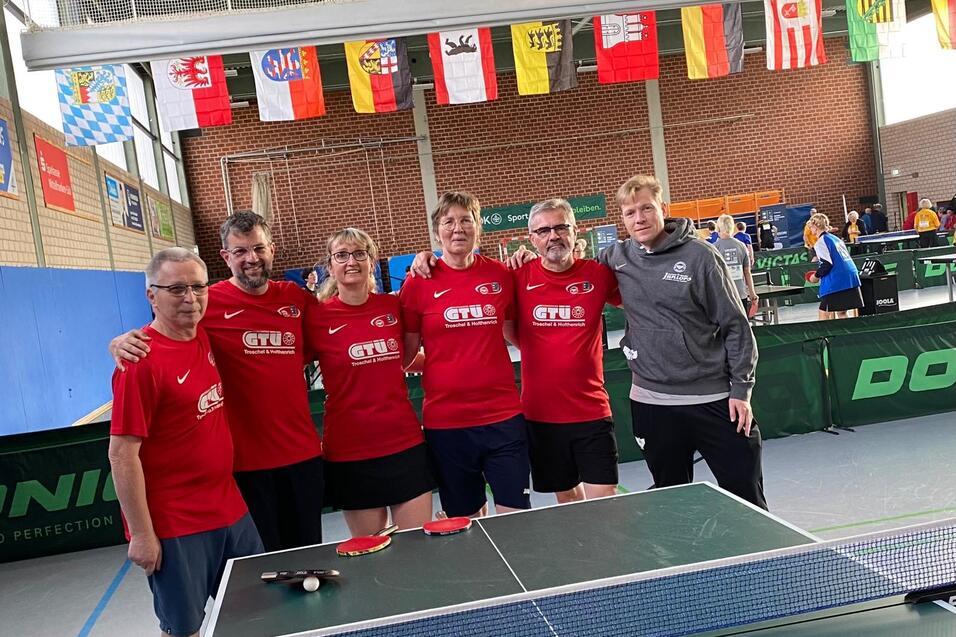 Gruppe von fünf Tischtennisspielern in roten T-Shirts posiert neben einem Tischtennistisch in einer Halle.
