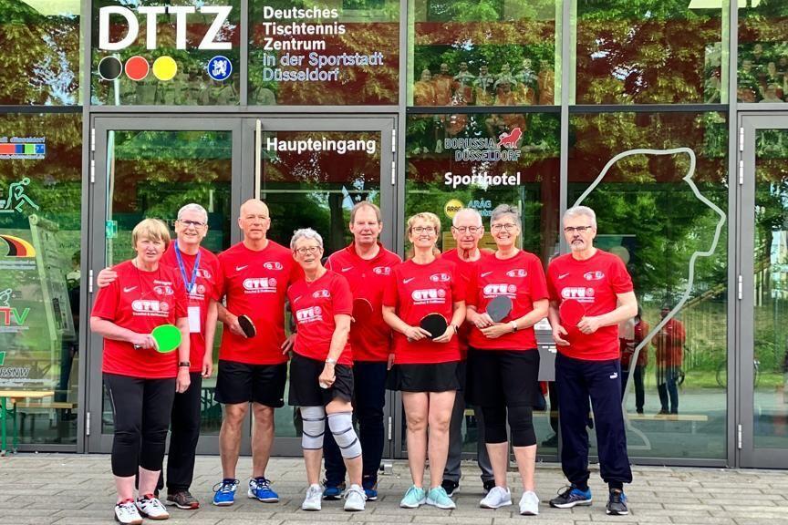 Eine Gruppe von sieben Tischtennisspielern in roten Shirts steht vor dem Deutschen Tischtennis Zentrum in D&uuml;sseldorf.