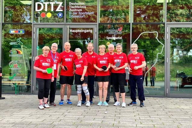 Eine Gruppe von sieben Tischtennisspielern in roten Shirts steht vor dem Deutschen Tischtennis Zentrum in D&uuml;sseldorf.