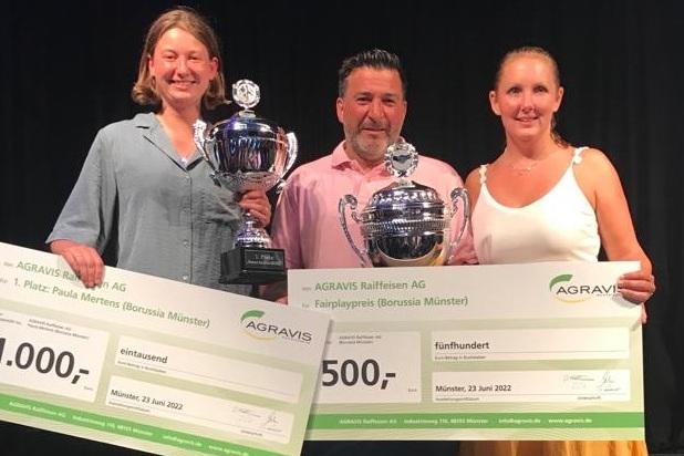 Drei Personen halten Pokale und Schecks f&uuml;r die Platzierungen bei einer Sportveranstaltung auf einer B&uuml;hne.