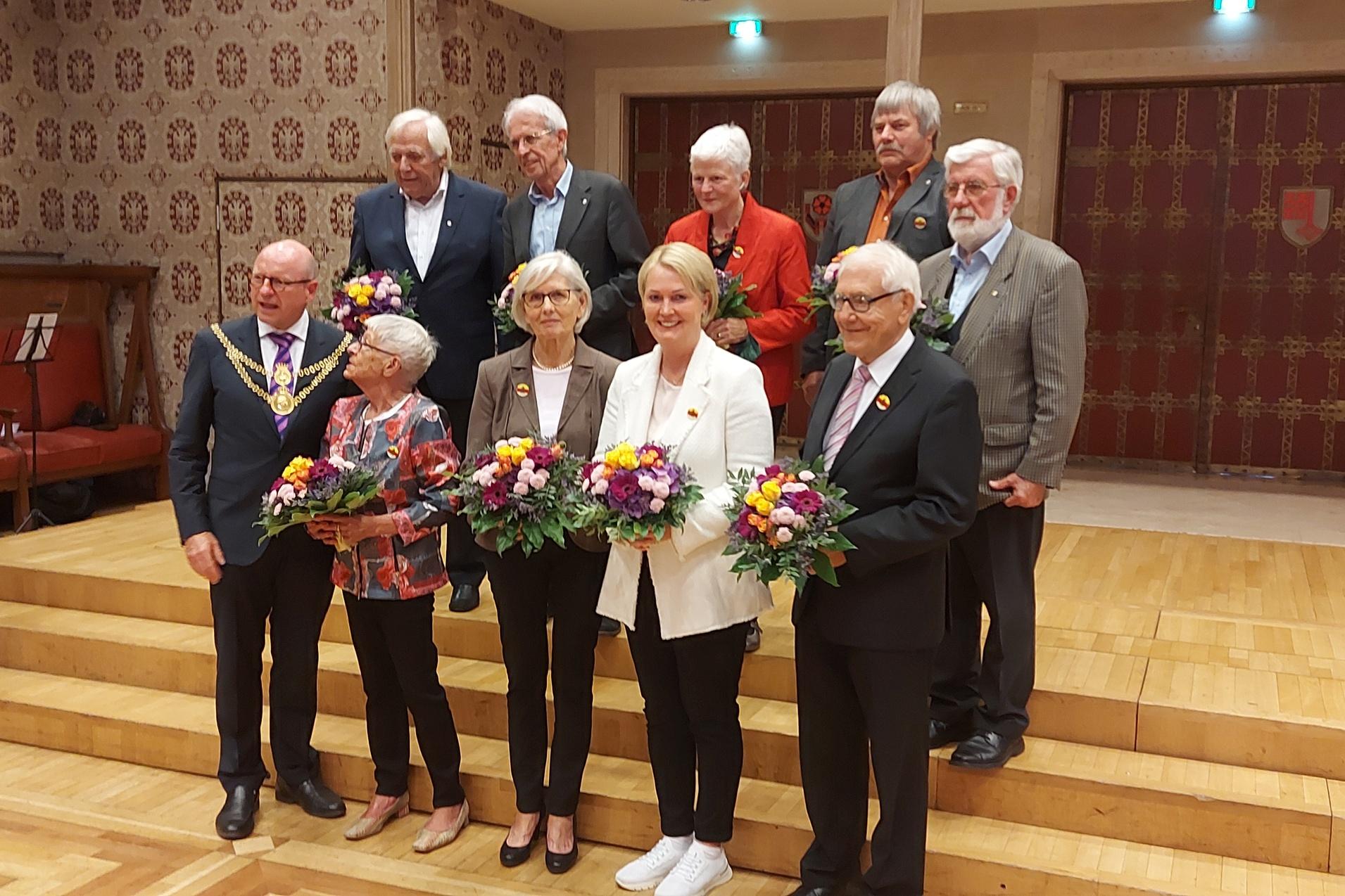 Gruppe von Personen mit Blumenstr&auml;u&szlig;en auf einer B&uuml;hne in einem festlichen Raum.