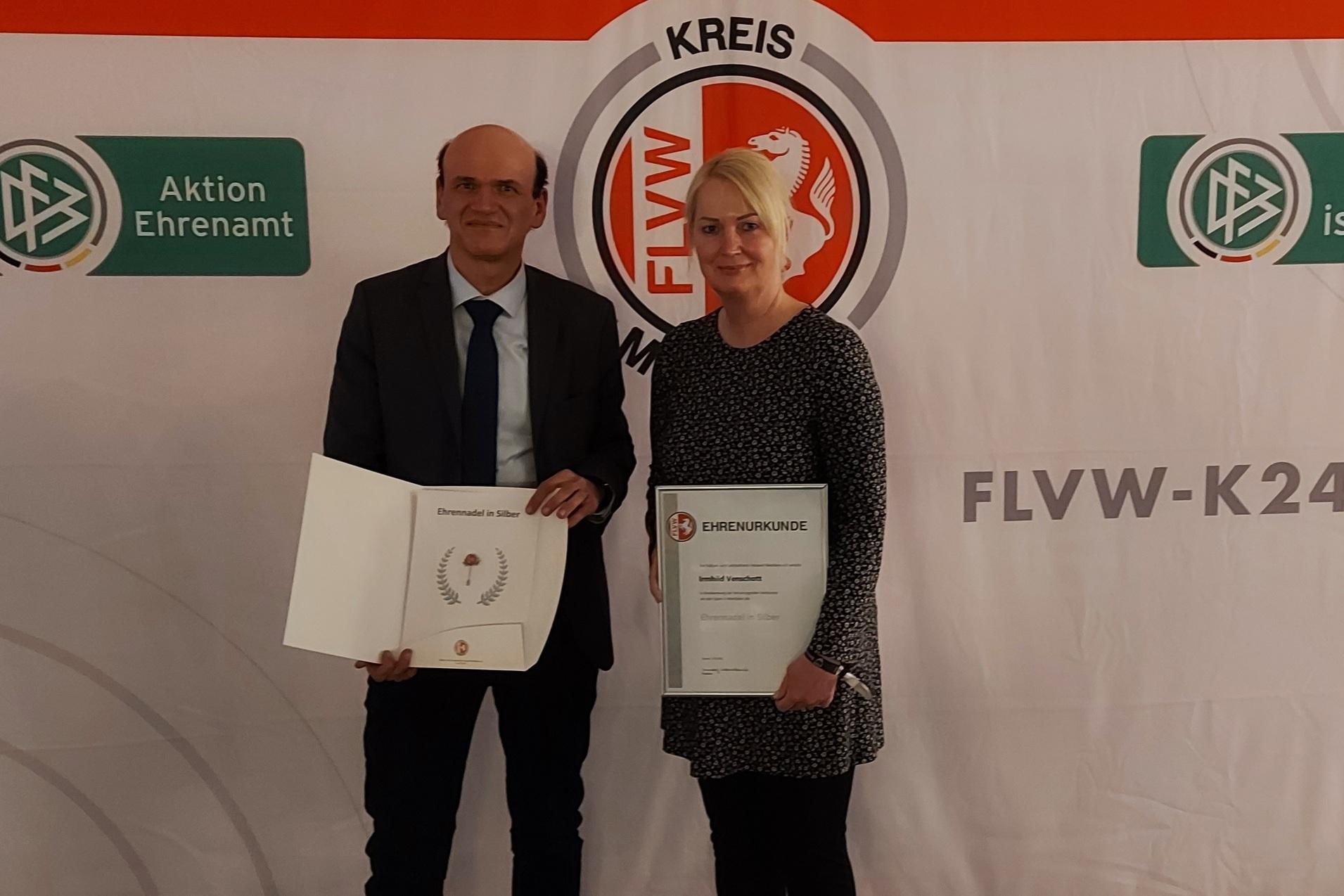Zwei Personen halten Zertifikate vor einem beschrifteten Hintergrund mit Logos und dem Schriftzug "FLVW-KREIS".