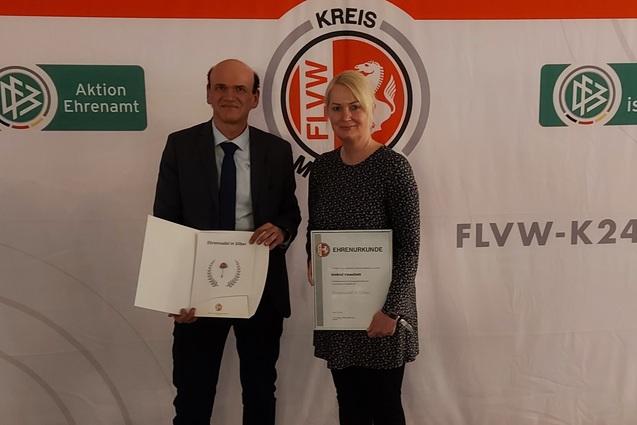 Zwei Personen halten Zertifikate vor einem beschrifteten Hintergrund mit Logos und dem Schriftzug "FLVW-KREIS".
