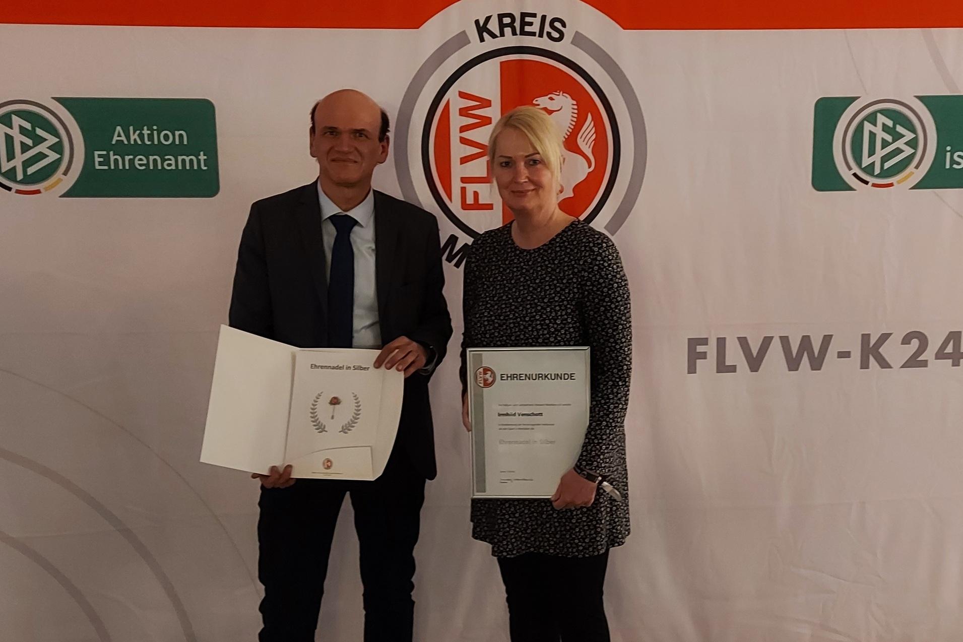Zwei Personen halten Zertifikate vor einem beschrifteten Hintergrund mit Logos und dem Schriftzug "FLVW-KREIS".