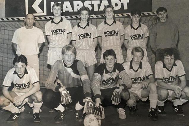 Schwarz-wei&szlig; Foto einer Fu&szlig;ballmannschaft mit Trainer, aufgestellt vor einem Tor mit &bdquo;Karstadt&ldquo;-Banner im Hintergrund.