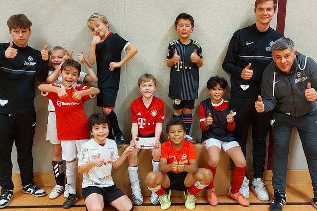 Eine Gruppe von Kindern und Trainern posiert l&auml;chelnd in einer Sporthalle, alle zeigen Daumen hoch.