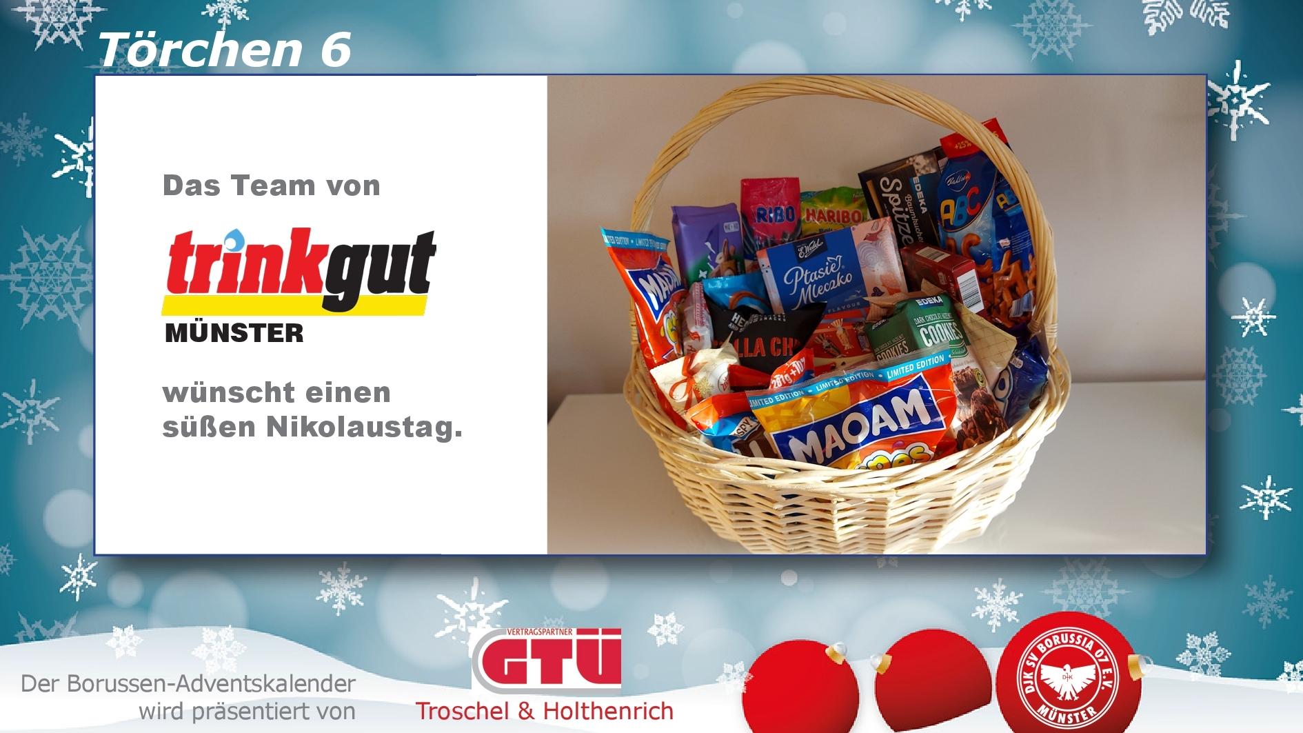 Korb mit S&uuml;&szlig;igkeiten und Snacks, umgeben von winterlichem Hintergrund, mit Gru&szlig; zum Nikolaustag von trinkgut M&uuml;nster.