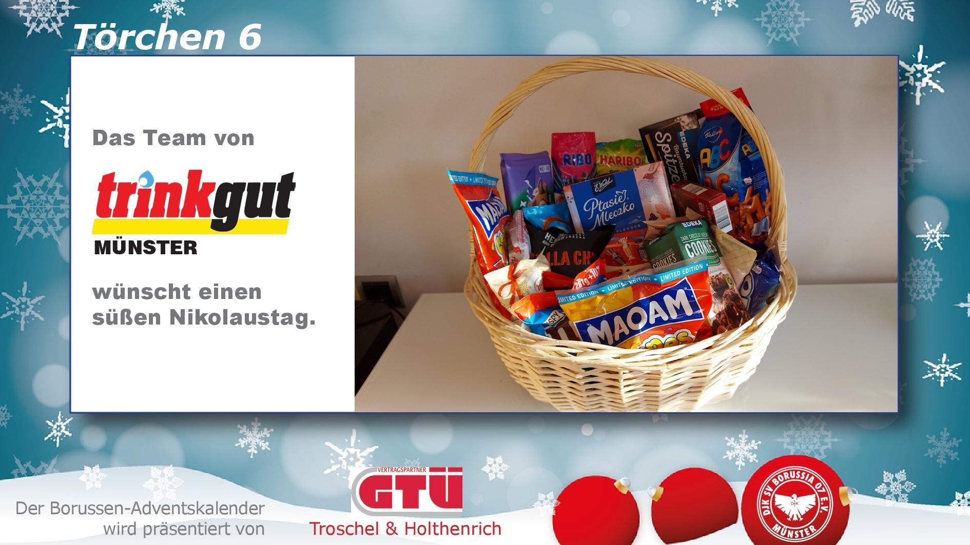 Korb mit S&uuml;&szlig;igkeiten und Snacks, umgeben von winterlicher Dekoration, mit Gr&uuml;&szlig;en des Teams von Trinkgut M&uuml;nster.