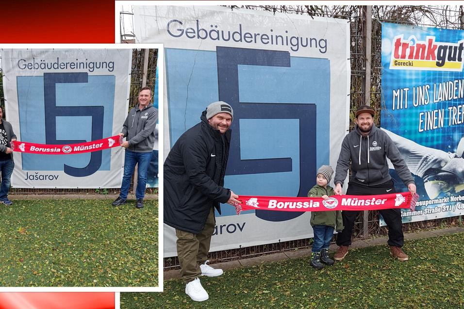 Drei Personen, darunter ein Kind, halten ein Fan-Banner von Borussia Münster vor einem Werbebanner.