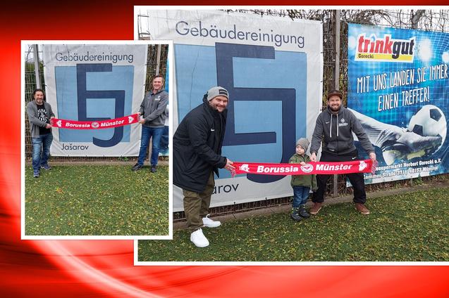 Drei Personen, darunter ein Kind, halten ein Fan-Banner von Borussia M&uuml;nster vor einem Werbebanner.