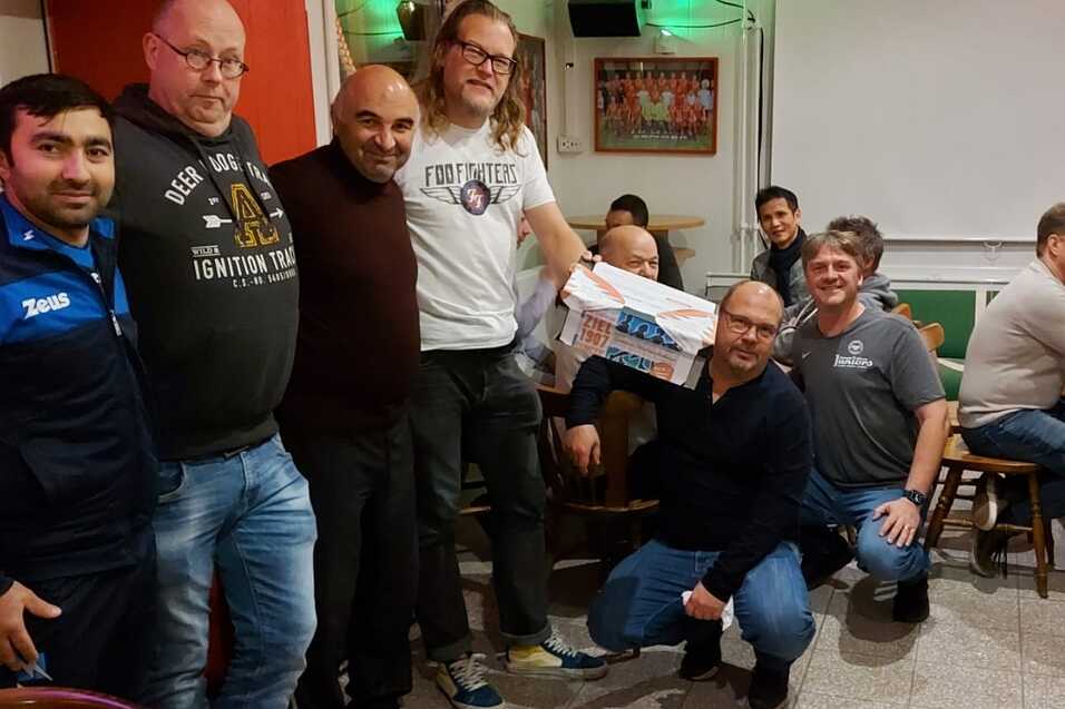 Gruppenszene in einem Restaurant mit zehn M&auml;nnern, einige halten ein Geschenk, andere sitzen am Tisch im Hintergrund.