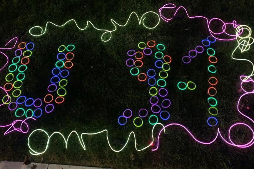 Bunte Lichter bilden die Zahlen 9-1-1 auf einer gr&uuml;nen Rasenfl&auml;che, umgeben von leuchtenden Ringen.