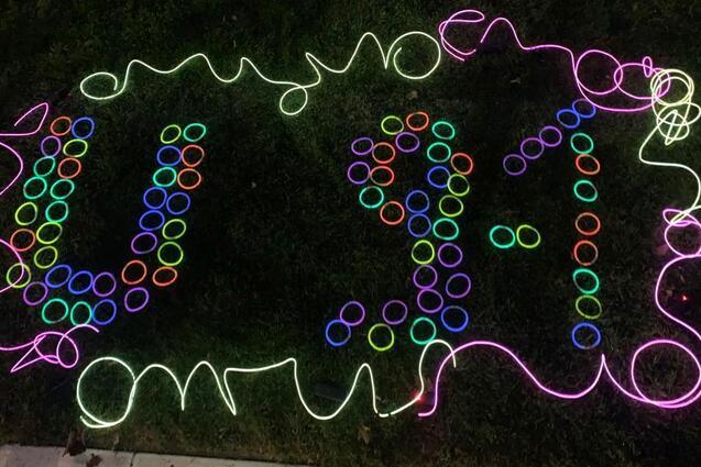 Bunte Lichter bilden die Zahlen 9-1-1 auf einer gr&uuml;nen Rasenfl&auml;che, umgeben von leuchtenden Ringen.