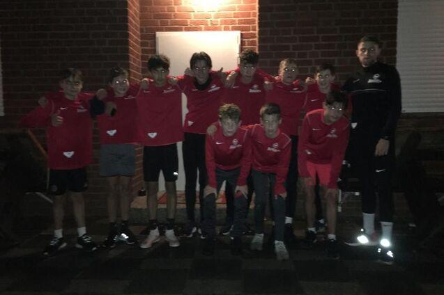 Gruppe von zehn Jugendlichen in roten Sweatshirts steht l&auml;chelnd vor einem Geb&auml;ude bei Nacht.