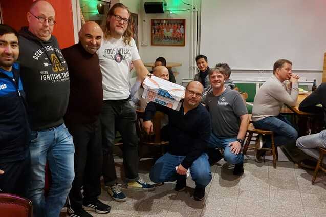 Gruppenszene in einem Restaurant mit zehn M&auml;nnern, einige halten ein Geschenk, andere sitzen am Tisch im Hintergrund.