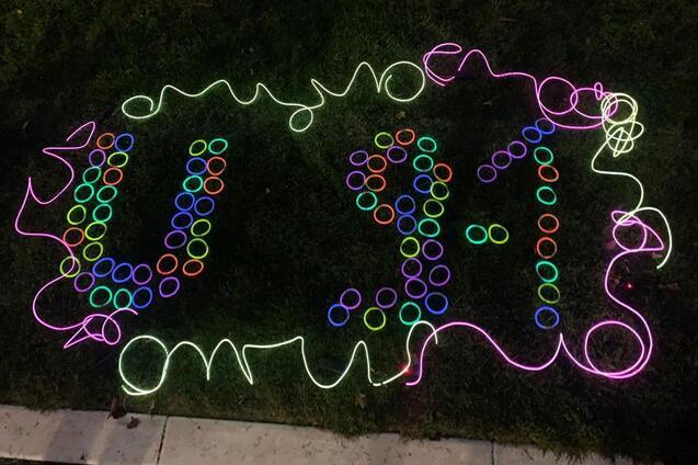 Bunte Lichter bilden die Zahlen 9-1-1 auf einer gr&uuml;nen Rasenfl&auml;che, umgeben von leuchtenden Ringen.