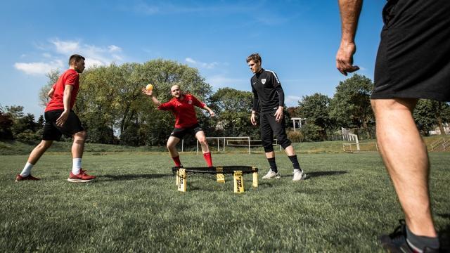 Vier Fußballspieler trainieren auf einem Rasenplatz, während einer einen Ball zu einem Mitspieler wirft.