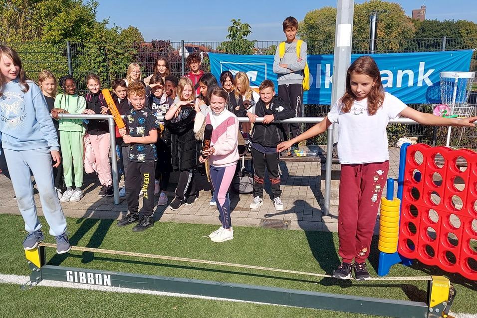 Gruppe von Kindern steht auf einer Slackline im Freien, einige lachen, w&auml;hrend andere zuschauen.