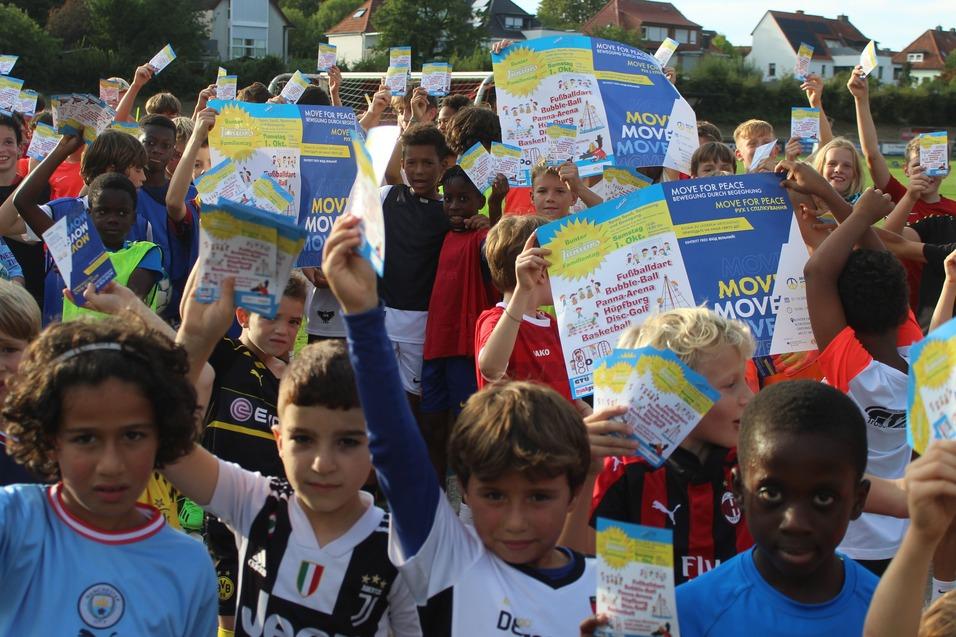 Grupp von Kindern in Sportkleidung h&auml;lt begeistert Flyer in die Luft, um eine Sportveranstaltung zu bewerben.