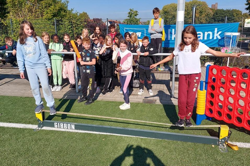 Gruppe von Kindern steht auf einer Slackline im Freien, einige lachen, w&auml;hrend andere zuschauen.