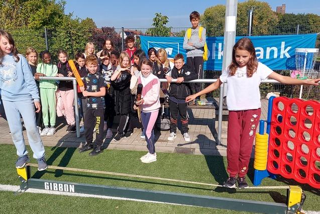 Gruppe von Kindern steht auf einer Slackline im Freien, einige lachen, w&auml;hrend andere zuschauen.