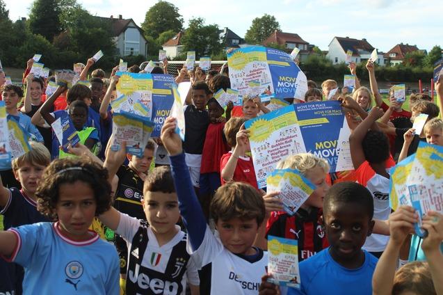 Grupp von Kindern in Sportkleidung h&auml;lt begeistert Flyer in die Luft, um eine Sportveranstaltung zu bewerben.