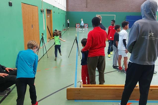 Gruppe von Kindern und Jugendlichen beim Training in einer Sporthalle, einige stehen, andere laufen, mit Ger&auml;ten und Zielen.