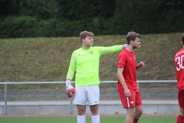 Zwei Fu&szlig;ballspieler stehen auf dem Platz; der Torwart in leuchtend gr&uuml;nem Trikot legt die Hand auf die Schulter eines Mitspielers.