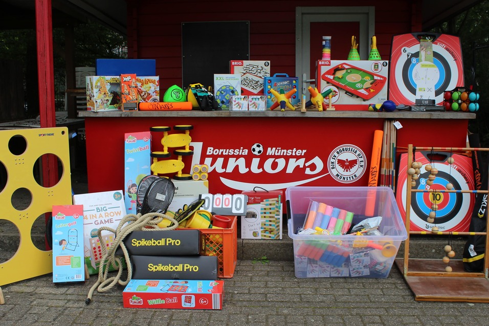 Bunte Auswahl an Spielzeugen und Sportger&auml;ten vor einem roten Stand mit dem Logo von Borussia M&uuml;nster Juniors.