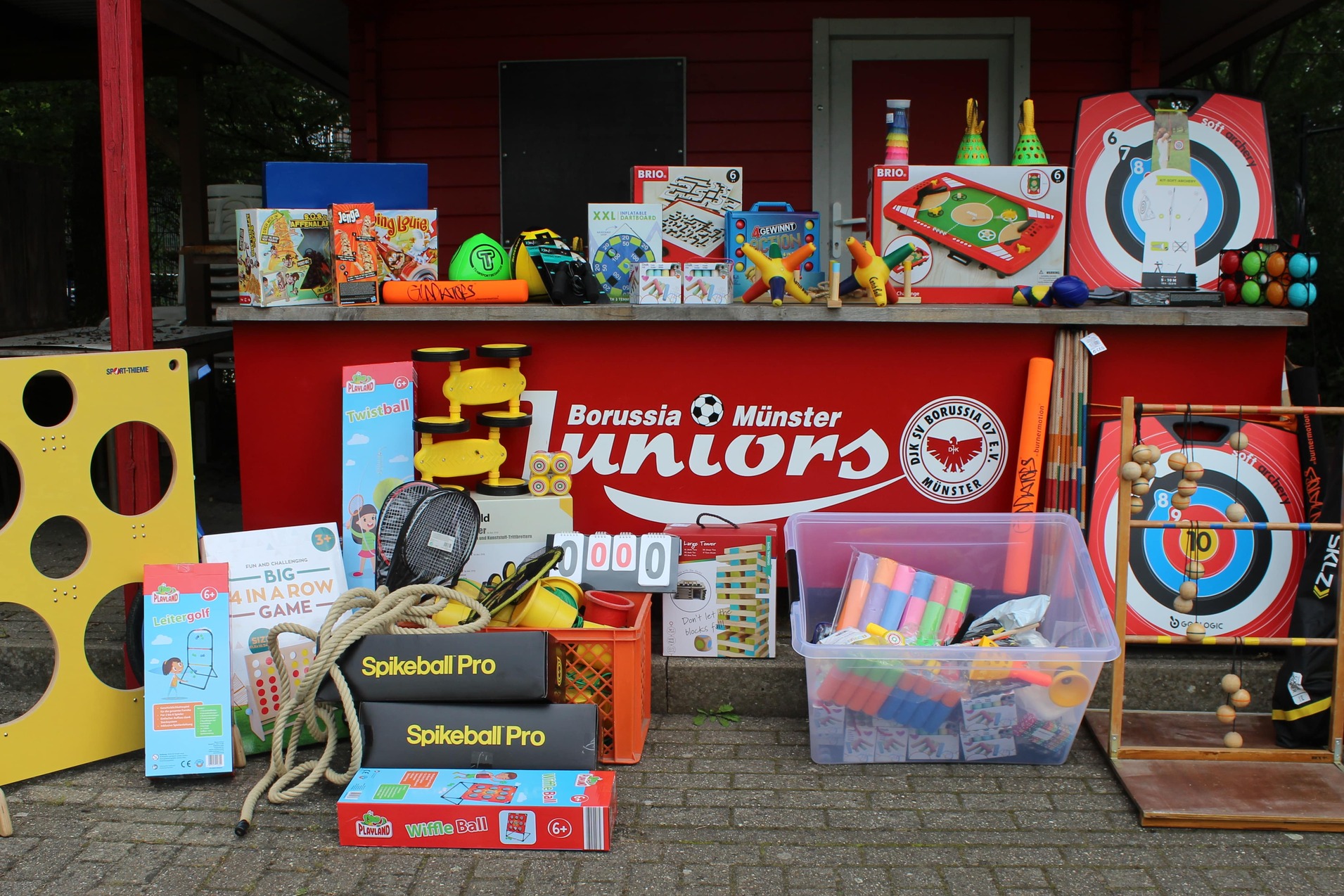 Bunte Auswahl an Spielzeugen und Sportger&auml;ten vor einem roten Stand mit dem Logo von Borussia M&uuml;nster Juniors.