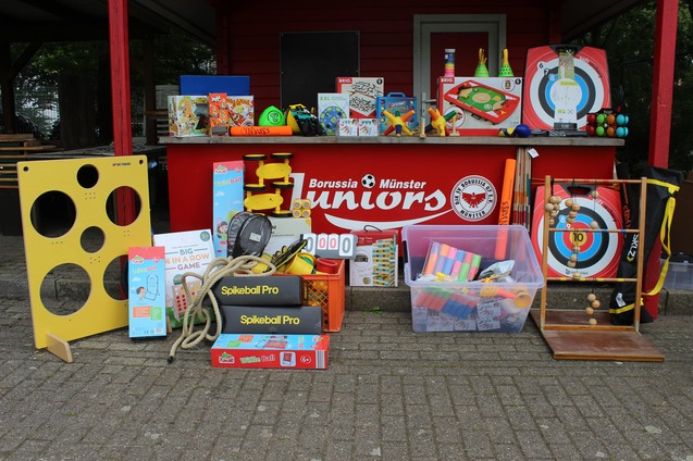 Bunte Auswahl an Spielzeugen und Sportger&auml;ten vor einem roten Stand mit dem Logo von Borussia M&uuml;nster Juniors.