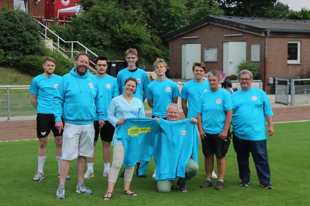 Gruppe von zehn Personen in blauen T-Shirts auf einem Sportplatz, lachend und posierend f&uuml;r das Foto.
