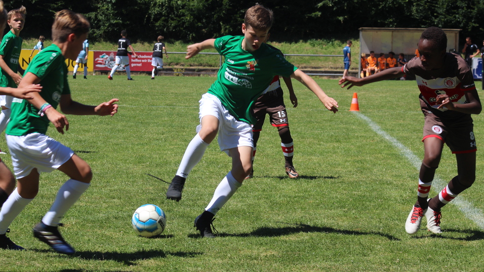 Jugendliche Fu&szlig;ballspieler in gr&uuml;nen und braunen Trikots dribbeln um den Ball auf einem Rasenplatz.