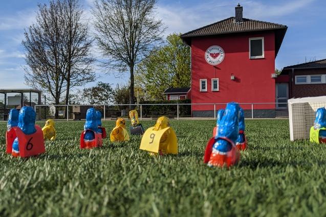 Bunte Spielfiguren in Form von Spielern stehen auf einem Fussballfeld vor einem roten Vereinsgeb&auml;ude.