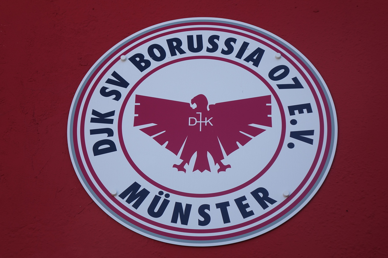 Vereinslogo von DJK SV Borussia 07 e.V. M&uuml;nster mit stilisiertem Adler auf rotem Hintergrund.