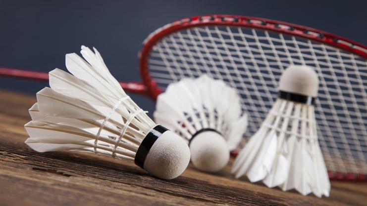 Drei Federbälle liegen auf einem Holztisch, mit einem Badmintonschläger im Hintergrund.