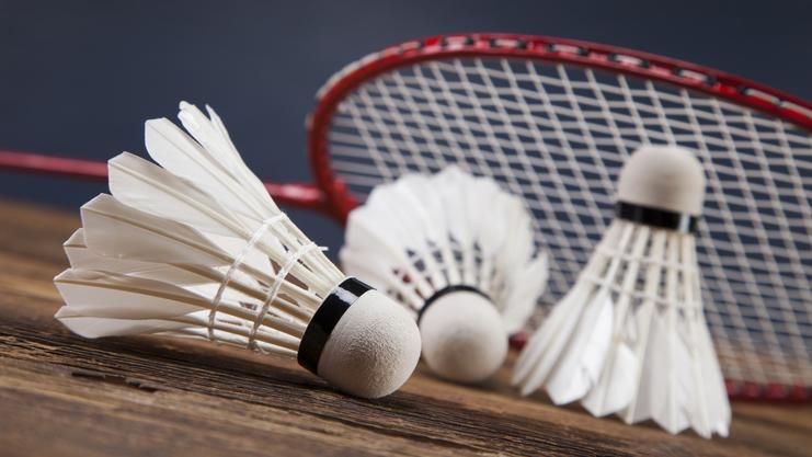 Drei Federbälle liegen auf einem Holztisch, mit einem Badmintonschläger im Hintergrund.