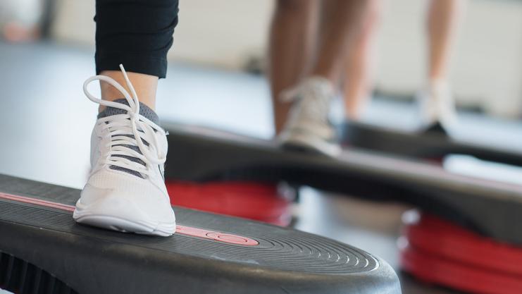 Nahaufnahme eines Fußs mit einem weißen Sport-Schuh auf einer Fitness-Stepp-Platte während eines Workout.