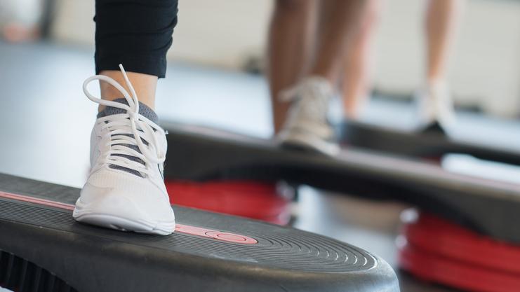 Nahaufnahme eines Fußs mit einem weißen Sport-Schuh auf einer Fitness-Stepp-Platte während eines Workout.