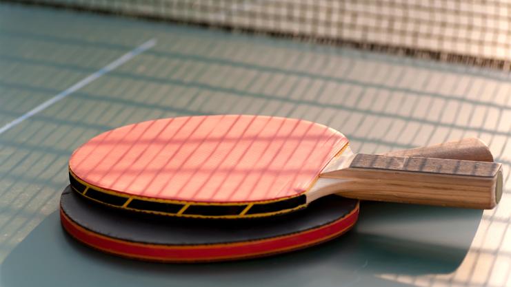 Nahaufnahme von zwei Tischtennisschlägern, einer mit roter und einer mit schwarzer Oberfläche, auf einer Tischtennisplatte.