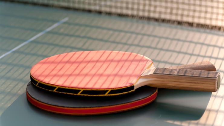 Nahaufnahme von zwei Tischtennisschlägern, einer mit roter und einer mit schwarzer Oberfläche, auf einer Tischtennisplatte.